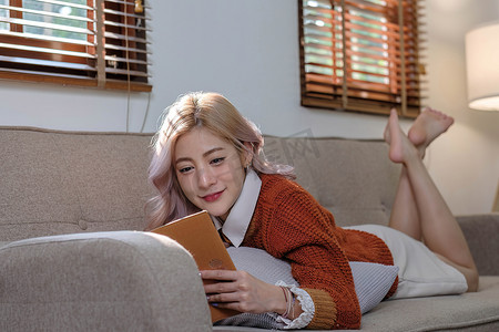 迷人的年轻亚洲女性坐在简约而舒适的客厅里，享受着读书的乐趣。