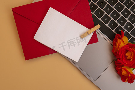 美丽的红玫瑰花在中性米色背景的邮政红包中，笔记本电脑键盘技术在线空白纸条复制空间文本，春天，节日贺卡。
