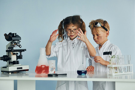 穿白大褂的小女孩和男孩使用设备在实验室扮演科学家