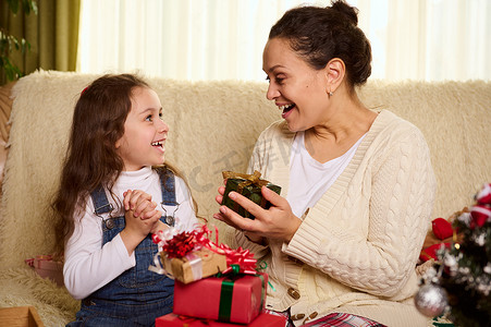 快乐慈爱的母亲和她可爱的小女儿表达积极的情绪，在交换圣诞礼物时欢欣鼓舞