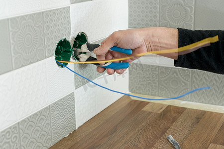 电工手用瓷砖在墙上安装插座的特写
