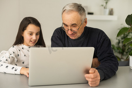 祖父和孙女花时间一起使用笔记本电脑，浏览网站，年轻一代教给年长者如何使用现代科技概念