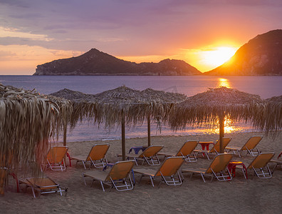 希腊科孚岛的 Agios Georgios Pagon 海滩上美丽的粉红色橙色日落，太阳伞空荡荡的日光浴床，享有波尔图蒂莫尼湾的景色