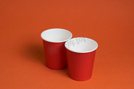 红色茶摄影照片_棕色背景上的两个红色一次性杯子。