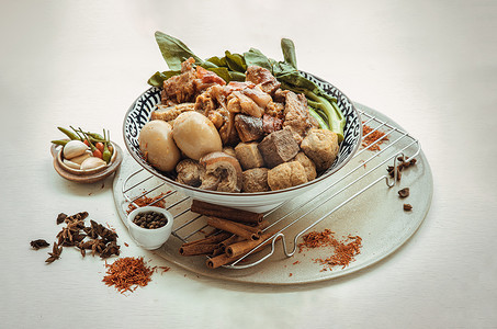 好吃的五花肉摄影照片_陶瓷碗中的炖猪腿、煮鸡蛋、豆腐和羽衣甘蓝，配以白色背景的大蒜和几内亚辣椒。