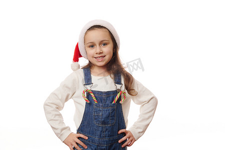 圣诞红摄影照片_漂亮的孩子，戴着圣诞帽的小女孩，在白色背景上与圣诞棒棒糖合影，并附有复制广告空间