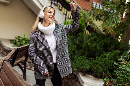 一位成年女性戴着耳机听音乐，并用手势向路人打招呼