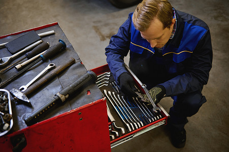 汽车修理工的顶视图，技术员从修理厂车库的盒子里拿扳手。