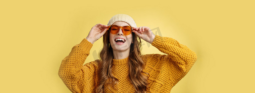 快乐时尚的白人女友享受阳光冬季滑雪胜地，戴着太阳镜帽子保暖毛衣，开心地笑着触摸眼镜，表达嬉戏的快乐心情黄色背景