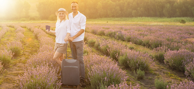 旅行箱背景摄影照片_男人和女人带着旅行箱在薰衣草田里，