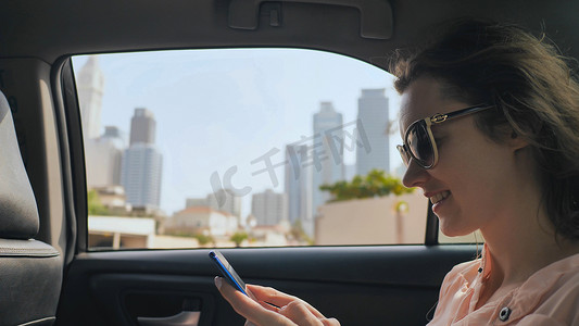 行驶着的汽车摄影照片_行驶中的汽车中，一个女孩正在用手机输入信息。