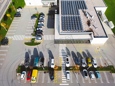 屋顶摄影照片_屋顶有太阳能电池板的现代办公楼前的停车场