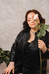 皮衣摄影照片_一位穿着黑色皮衣的时尚成年女性站着，室内有一束粉红玫瑰