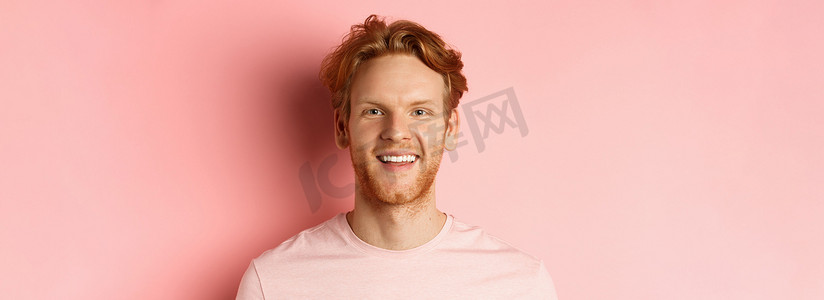 留着胡须和洁白牙齿的快乐红头发男人的头像，他对着镜头微笑，站在粉红色背景上