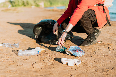 捡摄影照片_年轻的女志愿者满意地捡起垃圾、塑料瓶和咖啡杯，用大海清理海滩。