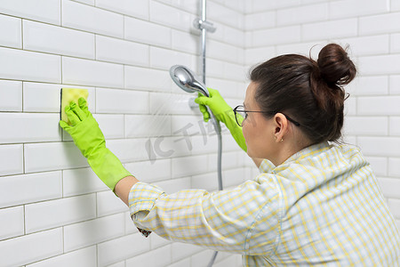 打扫浴室，女人用带洗涤剂的毛巾洗瓷砖墙