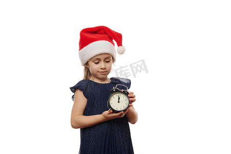戴着圣诞帽和晚礼服的可爱小女孩，手里拿着一个黑色复古闹钟，表盘上显示午夜。