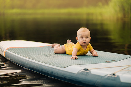 漂浮在水面上摄影照片_孩子躺在一个大的支撑板上漂浮在水面上。