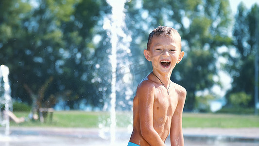 在炎热的夏日，七岁的兴奋男孩在喷水之间、在喷泉中、跑来跑去、洒水、玩得开心、玩得开心。