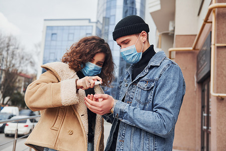 在检疫时间，在商业大楼附近的城市里，一对夫妇戴着防护面具，在户外使用防腐剂。