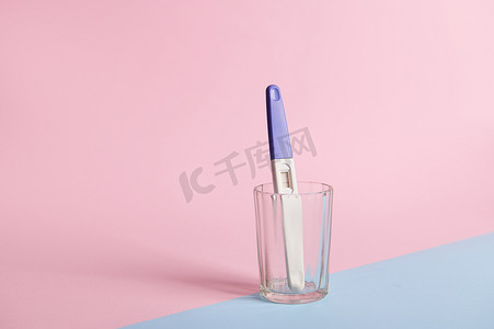 背景喷墨摄影照片_用两个条进行妊娠试验，在透明玻璃中显示阳性结果，隔离在粉红色和蓝色柔和的背景上。