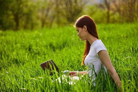 炎热的夏日，一位拿着笔记本电脑的女士坐在草坪上的城市公园里