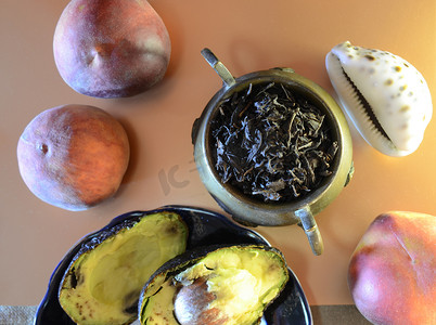 复古风格的甜点：盘子里有两半成熟的鳄梨、桃子、铜壶和大叶茶、椰子和贝壳组成