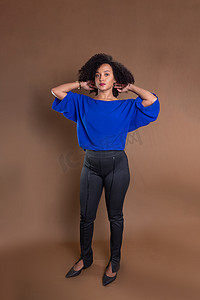 身穿蓝色衬衫的年轻女商人自信地站在棕色背景下。
