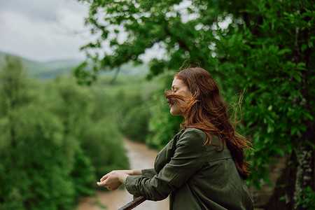 一个红头发随风飘扬的美女站在公园里俯瞰山河