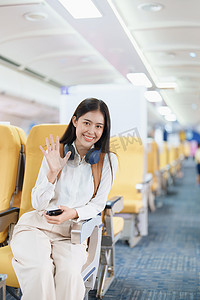年轻的亚洲美女乘飞机旅行，乘客戴着耳机把手提行李放在飞机座位上方的储物柜里
