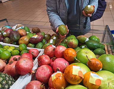 超市水果柜台摄影照片_来超市购物的特写女顾客，在柜台选择成熟的芒果和有机水果