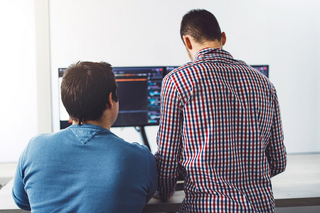 两个年轻的 IT 人员在电脑屏幕前写新代码的背影