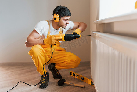 穿着黄色制服的杂工在室内使用锤钻工作。