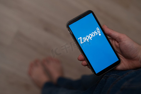 2022 年 12 月 3 日，哈萨克斯坦阿拉木图：赤脚妇女拿着带有 zappos 标志的智能手机。