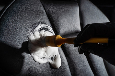 汽车内饰清洗摄影照片_使用刷子的泡沫和洗涤剂清洗皮革位子的过程。