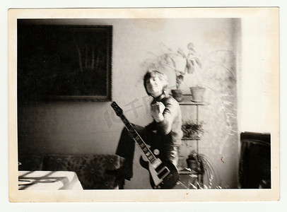 冷的男孩照片摄影照片_复古照片显示一个小男孩在弹吉他。