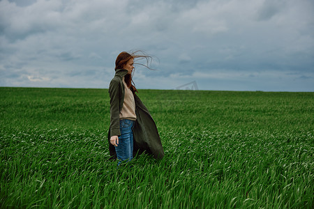 一个美丽的女人穿着雨衣站在绿色的田野里，眺望远方。