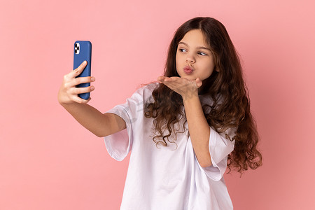 小女孩在通过视频通话、流媒体视频博客进行交流时，在智能手机摄像头上发送飞吻。