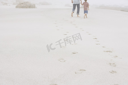 父子走在沙滩上留下脚印的后视图