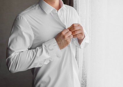 一个男人在窗外的光线下用手扣着白衬衫的纽扣