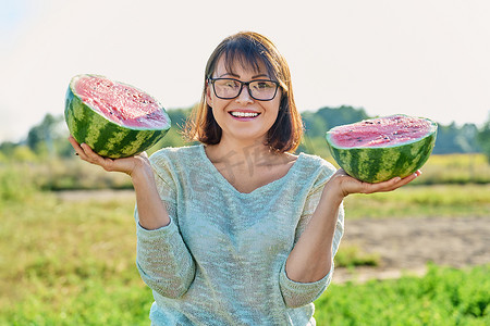 微笑的女人手里拿着半个成熟的西瓜，户外