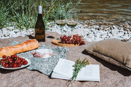 地毯花纹摄影照片_浪漫的乡村野餐，带两个白酒杯、瓶子、法式面包、奶酪、开放书