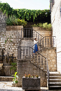 在黑山科托尔老城，一个身穿蓝色连衣裙、头戴草帽的女孩走在楼梯上。