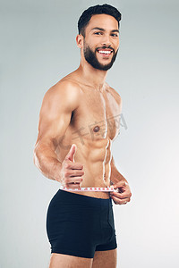 成功减肥摄影照片_身体、腰部和竖起大拇指，在灰色背景的工作室里与男模特一起，以促进减肥或锻炼。