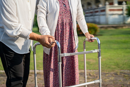 帮助和照顾亚洲老年或老年老妇人在愉快的新鲜假期里在公园散步时使用健康强壮的助行器。