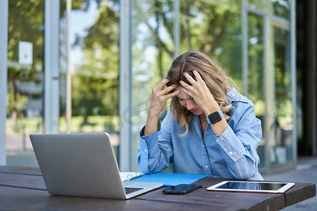 年轻职业女性坐在笔记本电脑旁，感到沮丧、失望的画像。