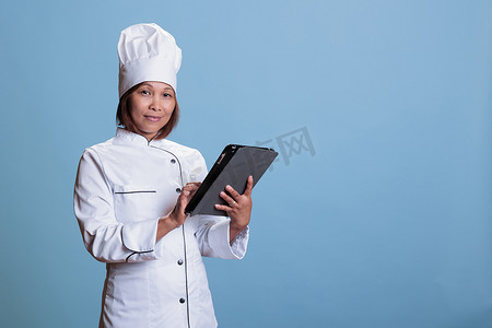 带围裙和白色制服的亚洲厨师手持平板电脑浏览菜谱