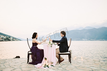 坐在海边摄影照片_男人和女人碰杯坐在海边码头的一张桌子旁