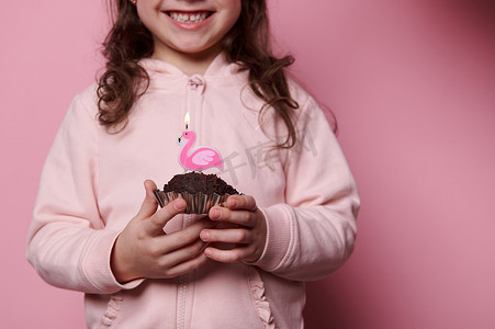 有选择地关注巧克力蛋糕，手里拿着火烈鸟蜡烛，生日女孩微笑着许愿