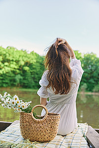 一位身穿浅色连衣裙的女性背对着镜头坐在湖岸边，拉直她的红发